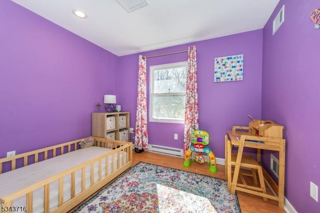 bedroom featuring wood finished floors, visible vents, baseboard heating, and baseboards