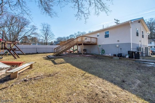 rear view of house with a deck, a playground, fence, a yard, and stairway