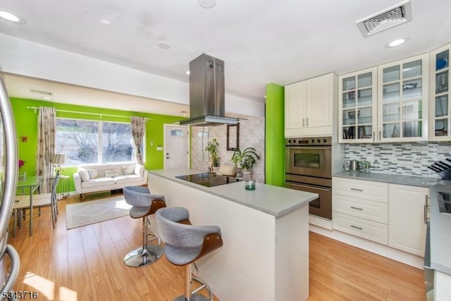 kitchen featuring visible vents, island exhaust hood, a kitchen breakfast bar, decorative backsplash, and black electric stovetop