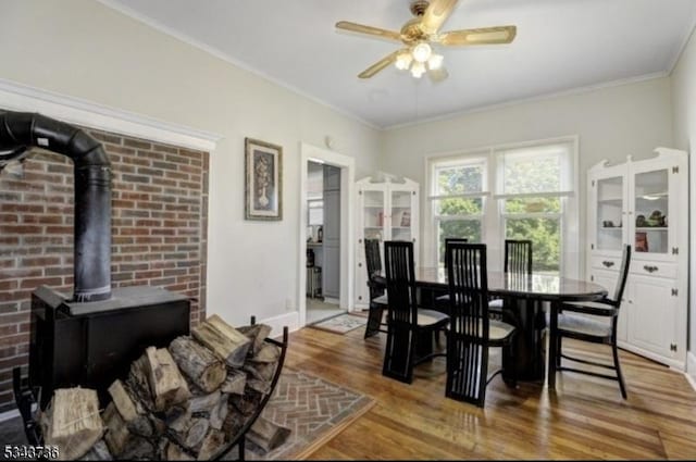 dining room featuring wood finished floors, crown molding, baseboards, ceiling fan, and a wood stove