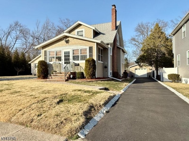 bungalow-style house with an outdoor structure, a garage, a front yard, and a chimney