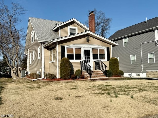 bungalow featuring central air condition unit, a chimney, a front yard, and roof with shingles