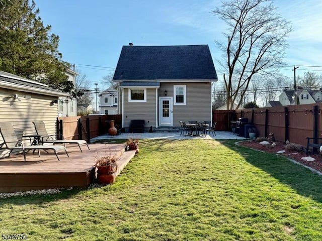 rear view of property featuring a fenced backyard, a wooden deck, a yard, and a shingled roof