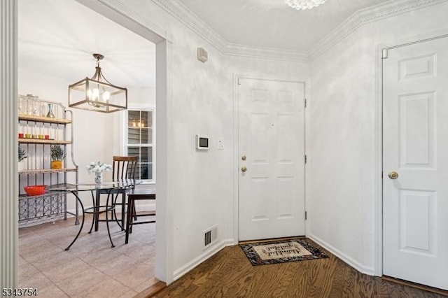 foyer entrance featuring visible vents, baseboards, an inviting chandelier, crown molding, and light wood-type flooring