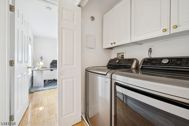 clothes washing area featuring light wood-type flooring, cabinet space, and washing machine and dryer