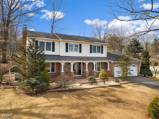 view of front of home with a front yard, driveway, an attached garage, covered porch, and a chimney