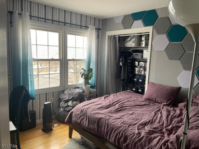 bedroom with wallpapered walls, wood finished floors, and a closet