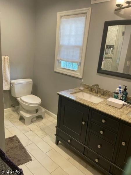 bathroom featuring double vanity, toilet, baseboards, and a sink