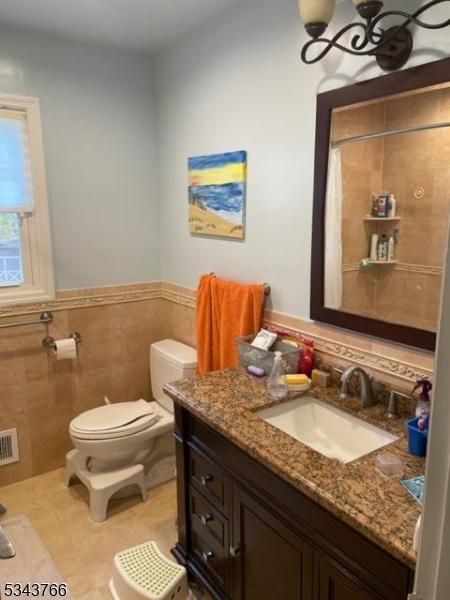 full bath with visible vents, a wainscoted wall, toilet, vanity, and tile walls