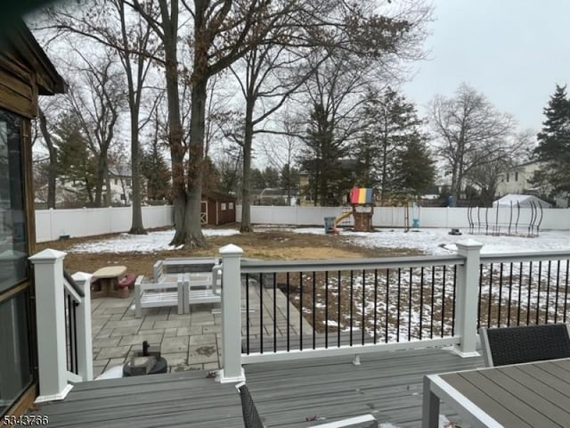 snow covered deck with outdoor dining area, a fenced backyard, and a playground