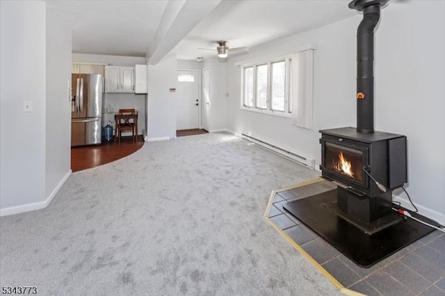 carpeted living area with baseboards, baseboard heating, ceiling fan, and a wood stove