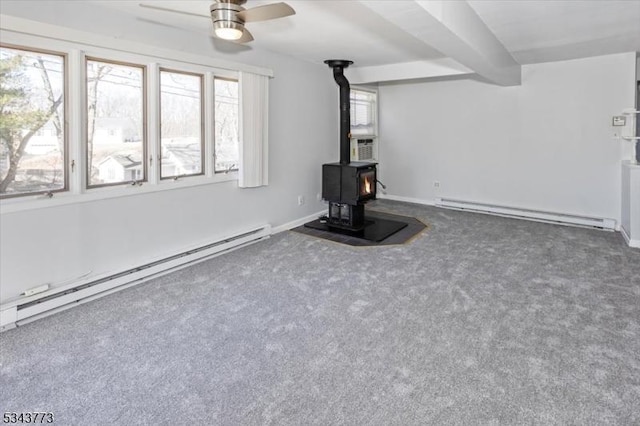 unfurnished living room featuring carpet flooring, a wood stove, ceiling fan, and a baseboard radiator