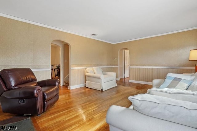 living room featuring a wainscoted wall, crown molding, light wood-style floors, and arched walkways