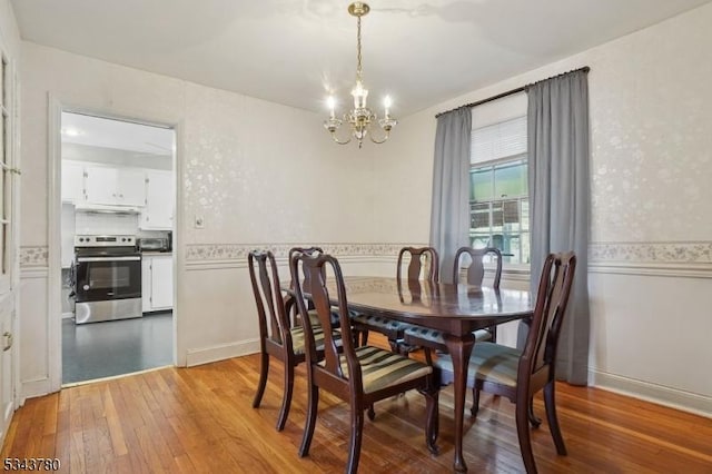 dining space featuring light wood-style flooring, a wainscoted wall, and a chandelier