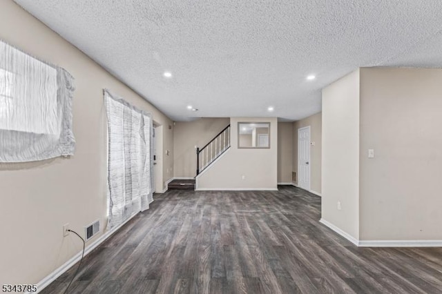 unfurnished living room with stairway, wood finished floors, baseboards, and a textured ceiling