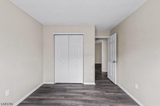 unfurnished bedroom with a closet, baseboards, a textured ceiling, and dark wood-style floors