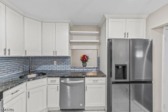 kitchen with backsplash, dark stone countertops, white cabinets, stainless steel appliances, and a sink