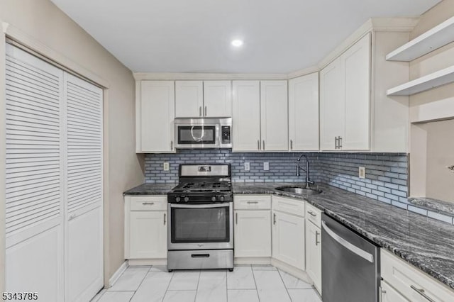 kitchen with a sink, stainless steel appliances, white cabinets, and dark stone countertops