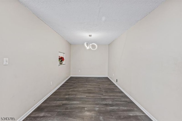 spare room with a notable chandelier, wood finished floors, baseboards, and a textured ceiling