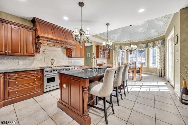 kitchen with an island with sink, a sink, a kitchen breakfast bar, premium range, and a chandelier