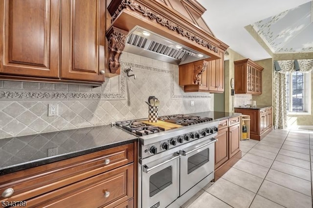 kitchen featuring light tile patterned flooring, brown cabinets, premium range hood, and range with two ovens