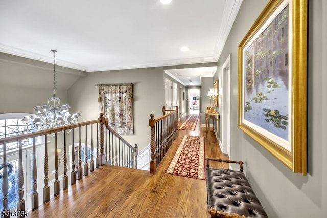 corridor featuring wood finished floors, baseboards, an inviting chandelier, ornamental molding, and an upstairs landing