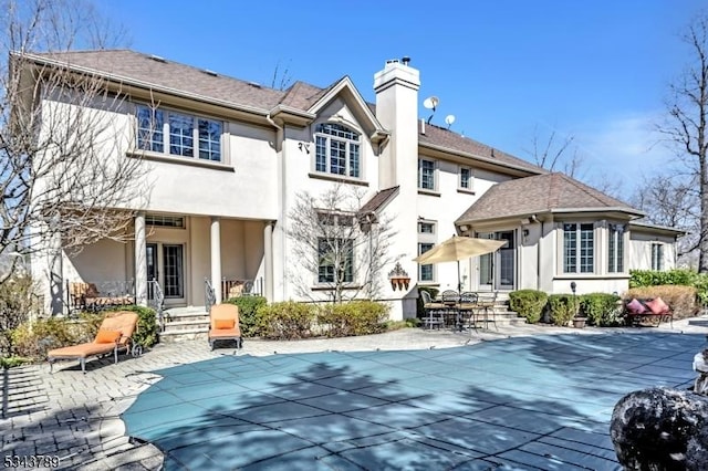 rear view of property featuring stucco siding, a patio, a chimney, and a covered pool