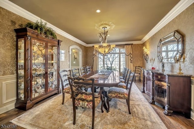 dining area featuring a notable chandelier, crown molding, wainscoting, and wallpapered walls