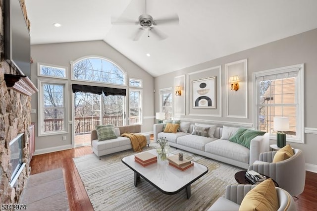 living area featuring baseboards, a fireplace, wood finished floors, high vaulted ceiling, and a ceiling fan