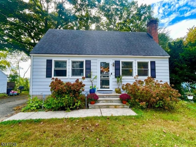 view of front of property with entry steps, a chimney, a front lawn, and a shingled roof