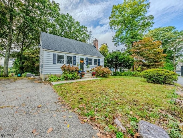 view of front of property with a front yard, a chimney, driveway, and roof with shingles