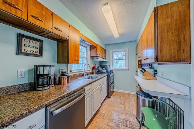 kitchen featuring dark countertops, under cabinet range hood, stainless steel appliances, a textured ceiling, and a sink