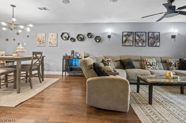 living room featuring ceiling fan with notable chandelier, wood finished floors, visible vents, and baseboards