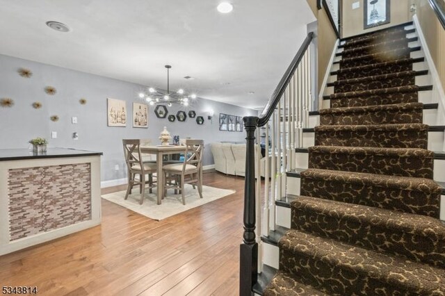 staircase with baseboards, an inviting chandelier, and hardwood / wood-style floors