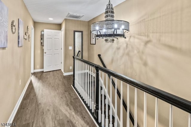 corridor with visible vents, baseboards, an upstairs landing, wood finished floors, and a notable chandelier