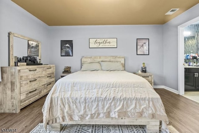 bedroom featuring connected bathroom, visible vents, baseboards, and wood finished floors