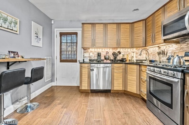 kitchen with dark countertops, backsplash, stainless steel appliances, and light wood-type flooring