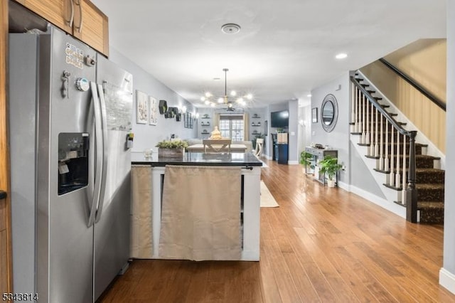 kitchen with wood finished floors, a peninsula, stainless steel refrigerator with ice dispenser, dark countertops, and open floor plan