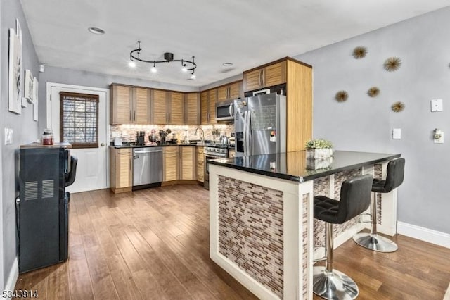 kitchen with dark countertops, a breakfast bar, decorative backsplash, hardwood / wood-style flooring, and stainless steel appliances