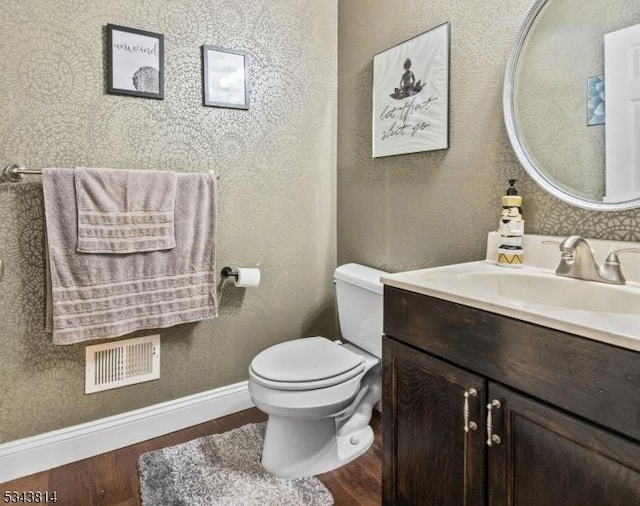 half bath with vanity, wood finished floors, visible vents, baseboards, and toilet