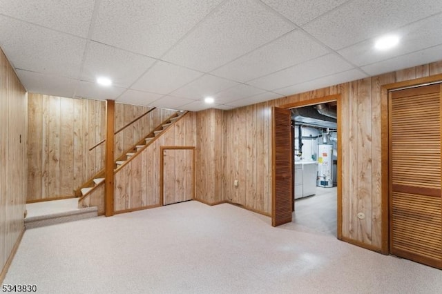 finished basement featuring wooden walls, stairway, carpet floors, recessed lighting, and gas water heater