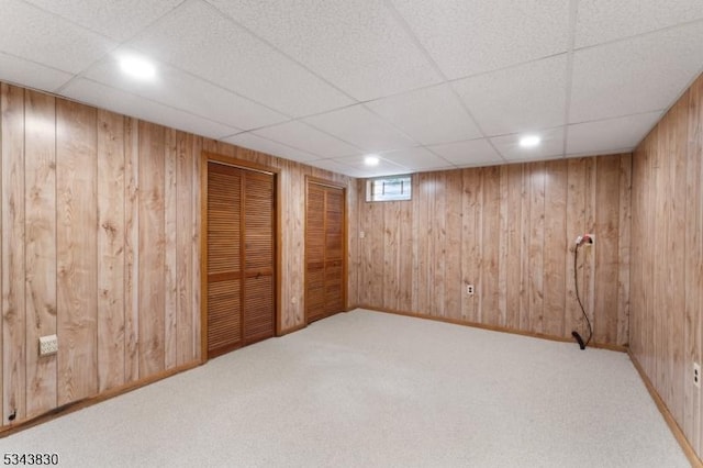 basement featuring carpet flooring, wood walls, and a drop ceiling