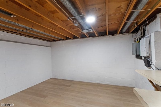 unfinished basement with electric panel, visible vents, light wood-type flooring, and water heater