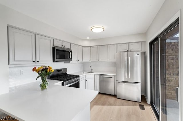 kitchen featuring light wood-type flooring, a sink, appliances with stainless steel finishes, a peninsula, and light countertops