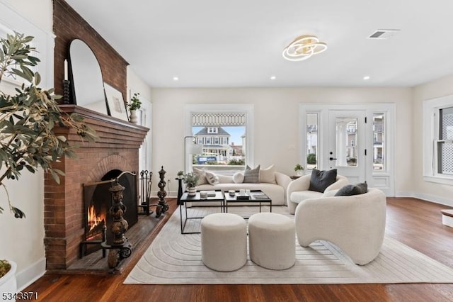 living area with a brick fireplace, wood finished floors, visible vents, and baseboards