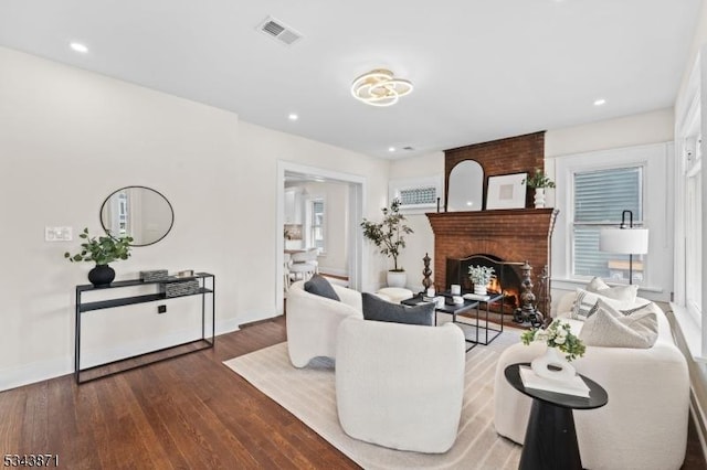 living room with visible vents, baseboards, a brick fireplace, and wood finished floors