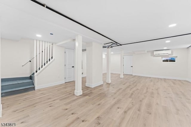 basement featuring light wood finished floors, stairway, a wall mounted air conditioner, and baseboards