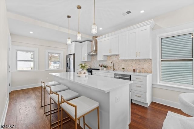 kitchen featuring visible vents, a breakfast bar, stainless steel appliances, wall chimney exhaust hood, and a sink