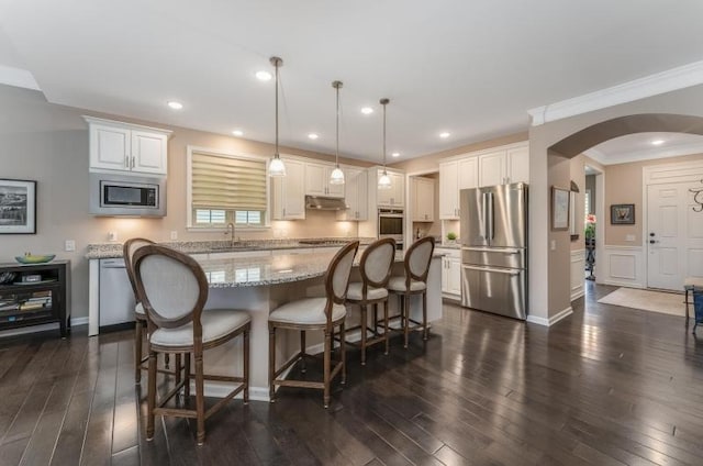 kitchen with a center island, under cabinet range hood, arched walkways, stainless steel appliances, and dark wood-style flooring