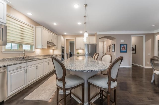 kitchen featuring baseboards, a sink, stainless steel appliances, under cabinet range hood, and a kitchen bar